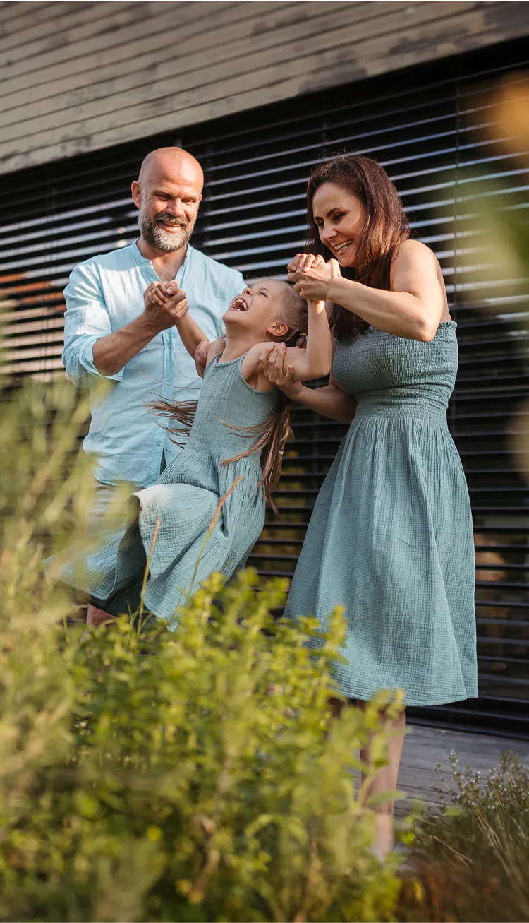 Fröhliche Eltern spielen vor einem Haus mit ihrem Kind.