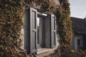 Vue rapprochée sur une fenêtre équipée d’un volet roulant solaire LAKAL et d’anciens volets battants